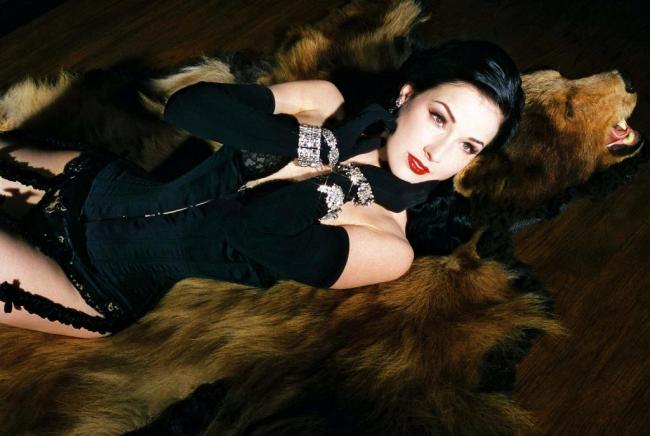 Dita von Teese taking a rest on her latest victim while wearing her opera gloves and corset